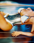 Woman in a white and silver latex bikini lying on a tanning bed
